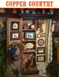 Cover photo of Stoney Creek Book 2 Copper Country cross stitch pieces displayed in a country cupboard MAIN