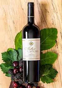 Nice bottle of Zinfandel laid atop an oak plank, with oak leaves and fruit accenting the photo. MAIN